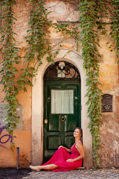A girl in a pink dress sitting in front of a green door with cream walls and cascading ivy. Taken by Rome Portrait Photographer, Tricia Anne Photography