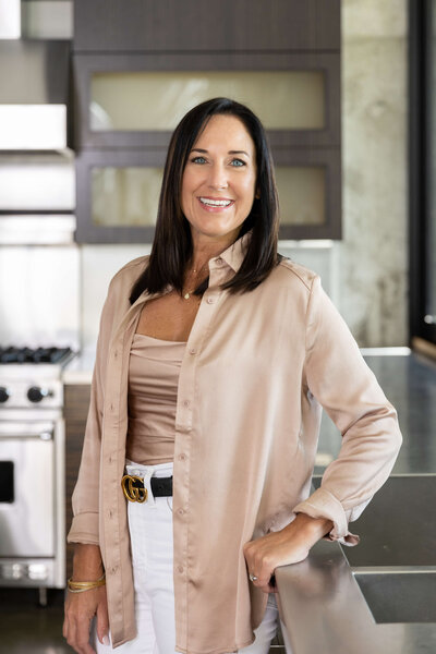 female realtor in white rolled up shirt in luxury kitchen with white carrera marble countertop writing with pen in notebook