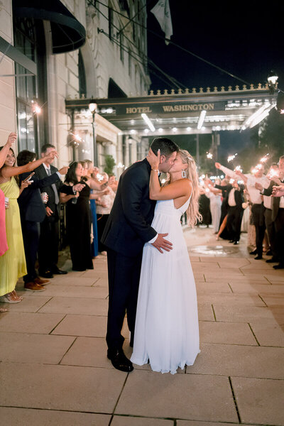Bride and groom kissing during their send off surrounded of sparkles with all their guests.