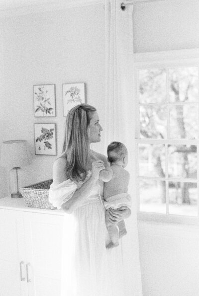 DC Maternity Photographer, Marie Elizabeth Photography,  holds newborn daughter and looks out the window.