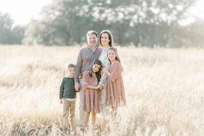 A family of 5 portrait taken while they are standing together while holding and snuggling eachother in a field at a local Dallas Texas park taken by a family photographer in Dallas TX.