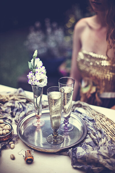 Woman in  evening dress in garden at table with vintage champagne glasses