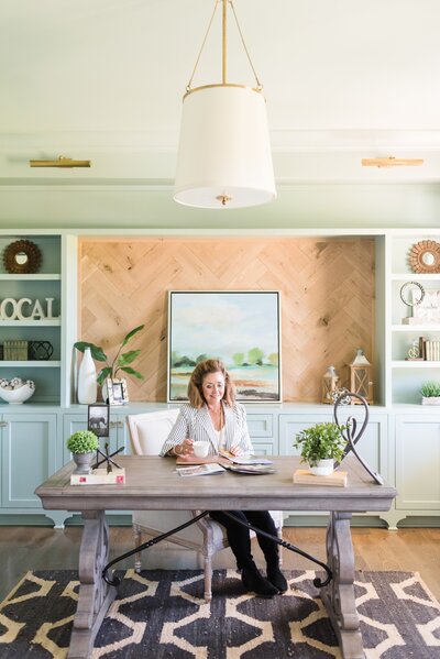 Nashville realtor sitting at her desk with a white coffee mug in her wood and seafoam office