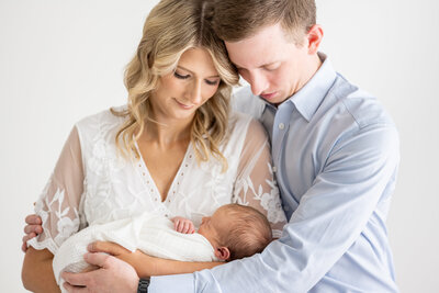 A new mother holding her baby while the father embraces them both
