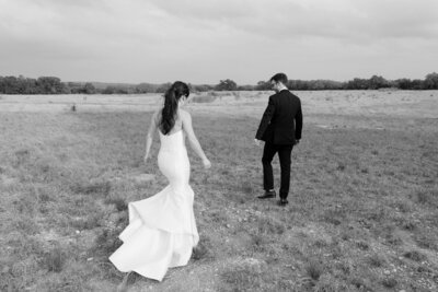 Black and white image of bride walking towards groom in a grassy field