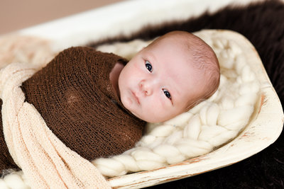 Beautiful Mississippi Newborn Photography: alert newborn boy wrapped in brown laying in dough bowl
