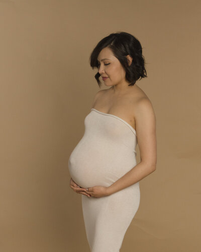 Shanna in a white dress showing her pregnant belly in an anne geddes inspired pose for her maternity photoshoot at the Fort Mill SC studio