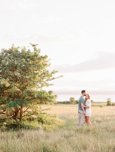 a man kissing his fiancé's forehead and she looks out into the distance at discovery park in seattle