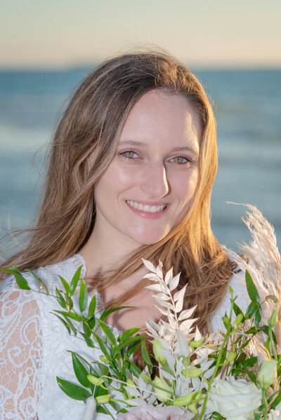 A bride holds her bouquet close to her face for a bridal portrait in front of the Gulf of Mexico.