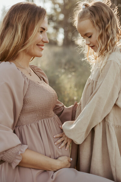 Pregnant mother watching her little girl touch her pregnant belly for their maternity photography session