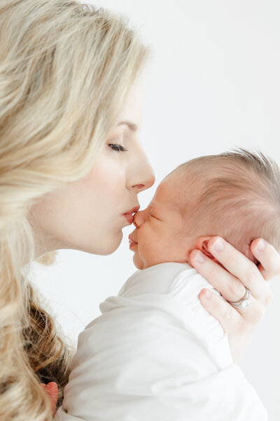 Close up of mother kissing her newborn baby's nose during newborn photography session