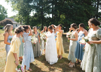 Bridesmaids fixing bride's veil while they all stand around her outside