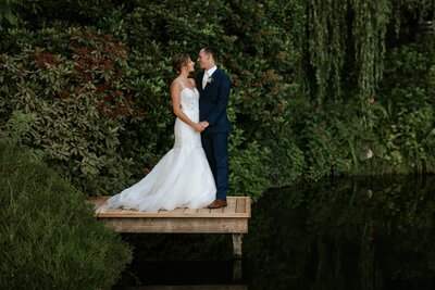 Bride and groom standing on a dock on a pond sharing moment captured by Tony Asgari