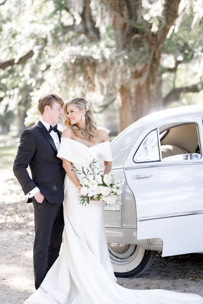 Couple standing with vintage car under spanish moss trees in Charleston South Carolina