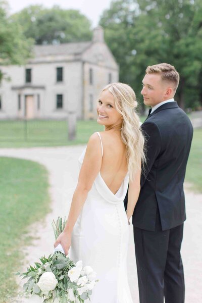 A bride and groom on their wedding day as the bride looks back at the camera and her groom looks at her