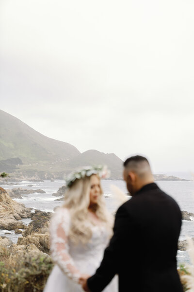 Sun-kissed couple exchanging vows on the sandy shores of Big Sur, with the vast ocean stretching to the horizon in the background