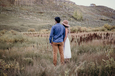 A couple stand holding hands in a field during their engagement photography session