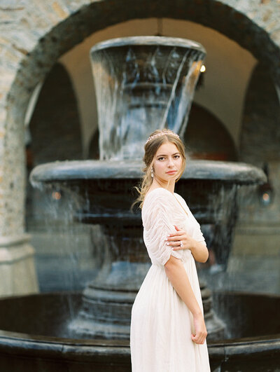 Bride standing in front of fountain looking over shoulder at camera
