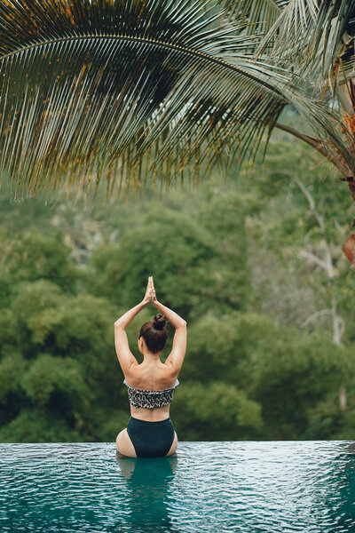 A woman sitting on the edge of a pool in an asana pose
