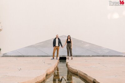Engaged couple hold hands while exploring the creek at Noguchi Gardens in Costa Mesa