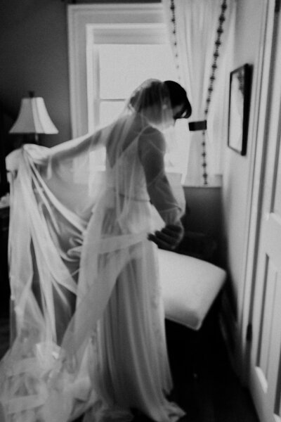 bride adjusting her long veil while getting ready, black and white photo