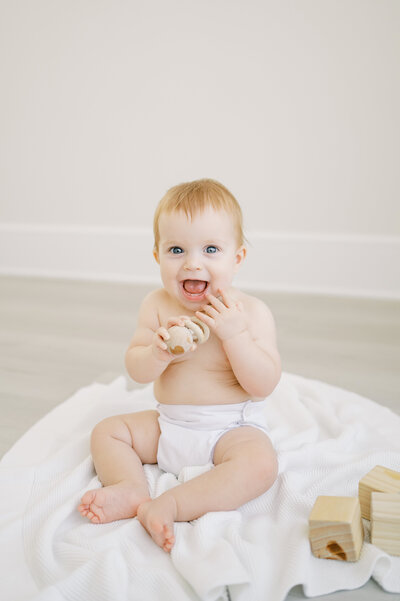 Baby boy in white diaper cover plays with wooden toys during baby photo session in Raleigh