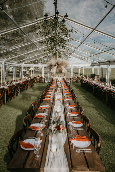 a clear tent with wooden tables and hanging greenery