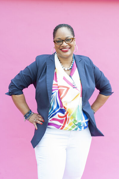 A woman stands smiling against a pink backdrop for a branding photo