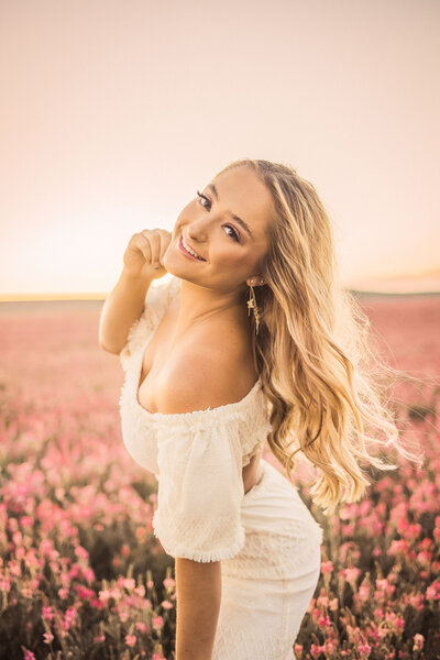woman with long blonde hair smiling in a field of pink flowers