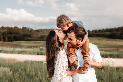 parents kissing while holding their son and daughter on dad's shoulders by Alyssum, Denver family and motherhood photographer