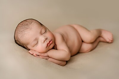 newborn boy is laying on his side with his hand under his cheek on a cream background