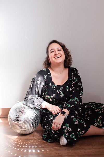 woman sitting on the ground smiling while resting one arm on a disco ball