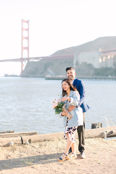 Couple engaged in Sausalito with Golden Gate Bridge view, girl holding flower bouquet, couple laughing, photo by Anastasiya Photography - San Francisco Photographer