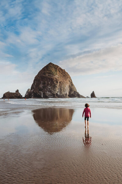 A landscape photograph of a girl walking on Cannon Beach on the Oregon coast