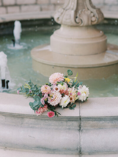 Soft blush and ivory wedding bouquet on the side of a water fountain