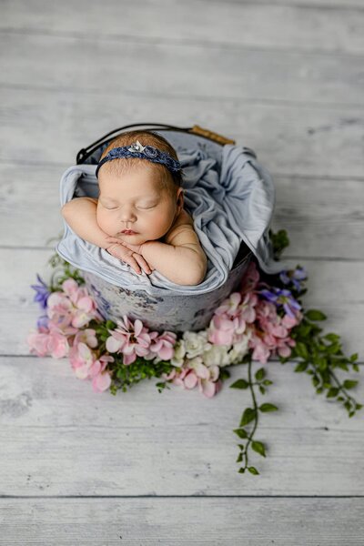 newborn baby girl portrait of infant wearing a blue bow and posed in a bucket surrounded by flowers