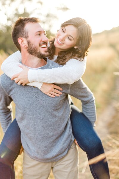 Man gives woman piggy-back ride through field during engagement session in Edina.
