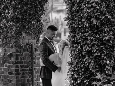 groom looks at bride lovingly surrounded by vines on an archway