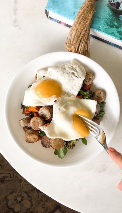 Bowl of greens, sweet potatoes, sausage, and fried eggs with a fork