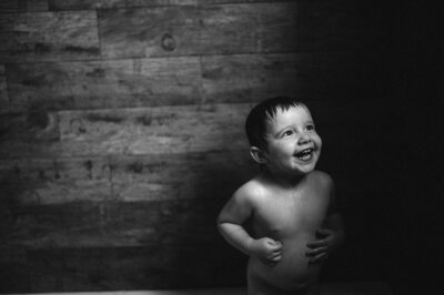 A black and white image of a  toddler in the bath