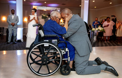 A person on their knees touching foreheads with someone in a wheelchair