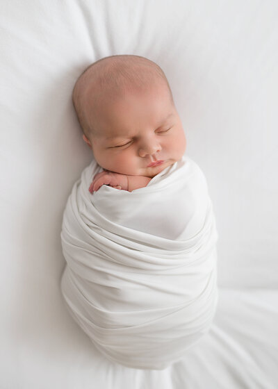 Newborn baby wrapped in white swaddle sleeps during Atlanta Newborn Photography Session.