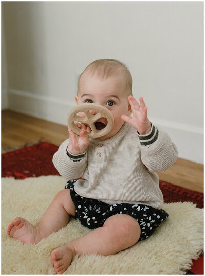 Baby sitting on fluffy rug with teething ring at  sweet at home family session in Austin by Amber Vickery Photography