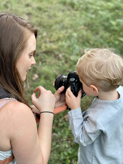 a child photographer bends down to show the photo on the digital camera to toddler client