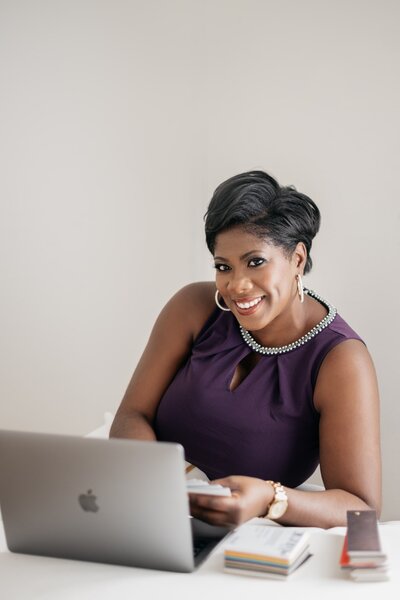 wedding planner in purple dress smiles while working at computer