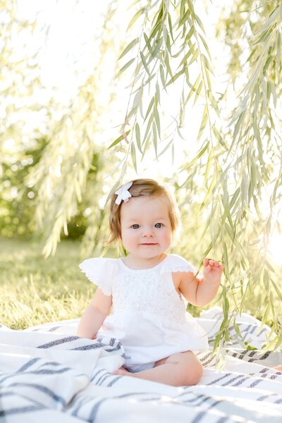 Infant sits in a field by willow tree for Minneapolis family portraits.