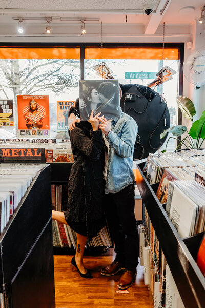 a cute couple standing in a record store holding up a record or Yoko Ono and  John Lennon in front of their faces