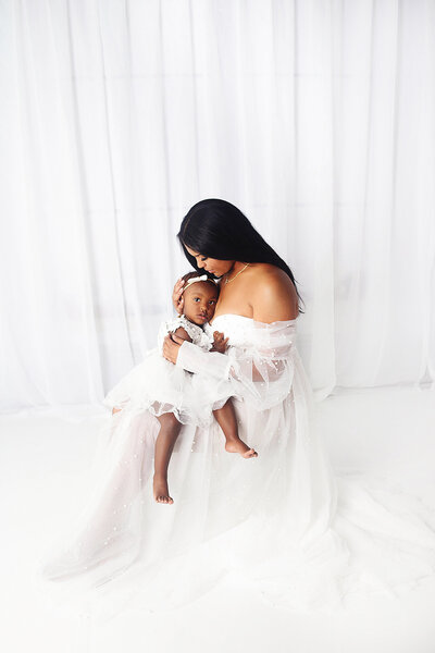 mother wearing white gown, holding daughter wearing white gown during mommy and me photoshoot in Brentwood Tennessee photography studio