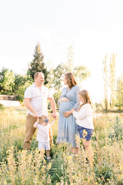 photo of young family standing in field playing with each other and mom wearing blue dress taken by Sacramento Newborn Photographer Kelsey Krall