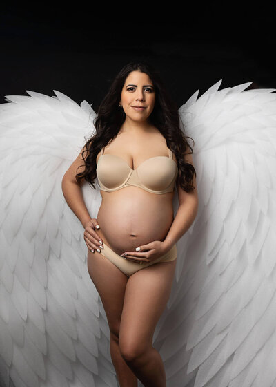 dark hair, pregnant woman wearing white wings for her maternity photoshoot in Austin, Texas